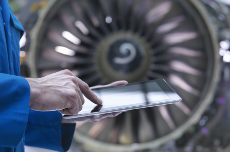 Aircraft engineer using a tablet with a commercial aircraft engine in the background.